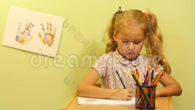可爱的女孩画画。 儿童手掌`彩色指纹。 女孩坐在桌子旁画画